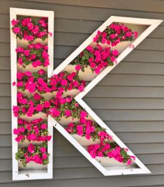 the letter k is decorated with pink flowers and hanging from it's sides in front of a gray house