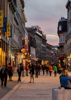 many people are walking down the street at dusk in an old european city with tall buildings