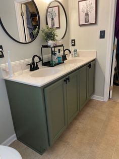 a bathroom with two sinks, mirrors and pictures on the wall above them is shown