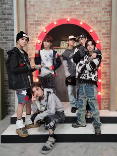 group of young men posing for photo in front of brick wall with neon lights behind them