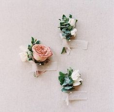 three boutonnieres with flowers on them sitting on a white tablecloth covered surface