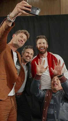 three men are taking a selfie with their cell phone while standing in front of a black backdrop