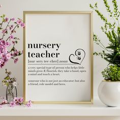 a white vase with pink flowers next to a framed poster that says nursery teacher on it