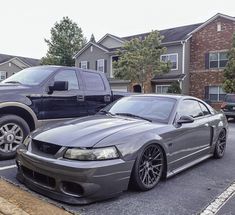 a gray mustang parked in a parking lot next to a black truck and some houses