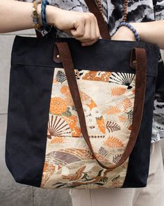 a woman holding a large black and orange tote bag in her hands with the handles down