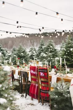 a dining room table set for christmas dinner with plaid chairs and lights strung from the ceiling