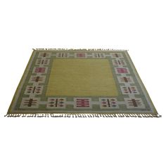 a green and yellow rug with fringes on the bottom, in front of a white background