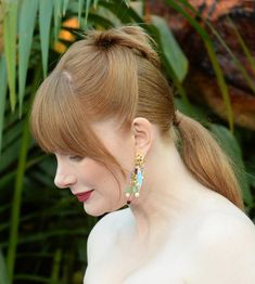 a woman with red hair wearing earrings and posing in front of some plants at an event