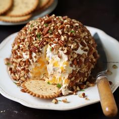 a cheese ball covered in pecans on a plate with crackers next to it