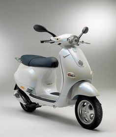 a white scooter is parked in front of a gray background