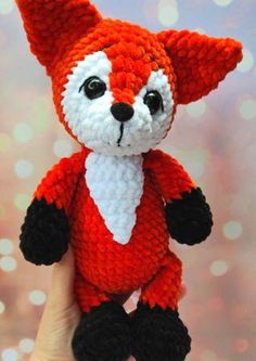 a hand holding a red and white knitted fox stuffed animal with black legs, tail, and nose