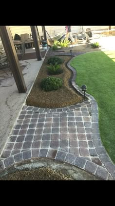 a brick walkway with grass and plants in the center, leading to a patio area