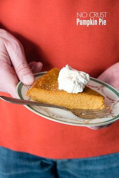 a person holding a plate with a slice of pumpkin pie on it and whipped cream on top