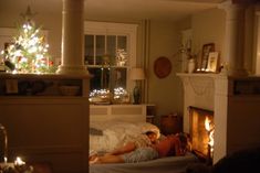 a person laying on a bed in front of a fire place with a christmas tree