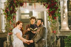 a man and woman are getting married in front of an arch decorated with red flowers