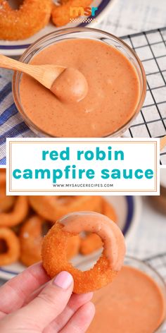 a hand holding a doughnut in front of a bowl of red robin campfire sauce