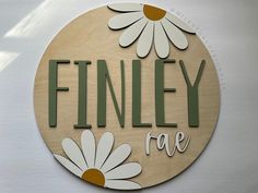 a wooden sign with daisies and the words finnley rae written in cursive letters