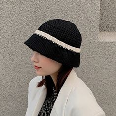 a woman wearing a black hat and white jacket standing in front of a gray wall