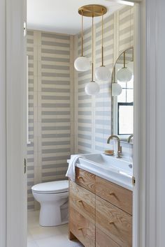 a white toilet sitting next to a bathroom sink under a mirror on top of a wooden cabinet