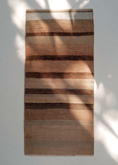 a brown and black striped rug against a white wall with shadow on the floor behind it