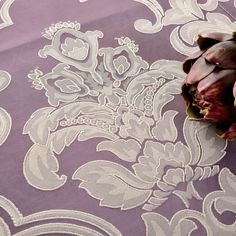 a flower laying on top of a purple and white table cloth with an intricate design