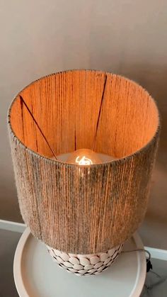 a lit candle sitting on top of a white plate next to a brown lamp shade