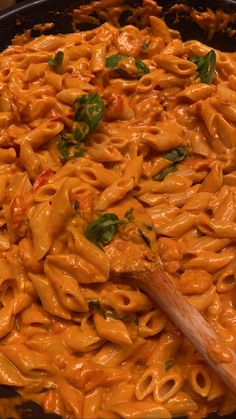 a skillet filled with macaroni and cheese being stirred by a wooden spoon