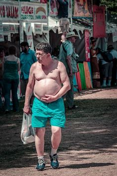 a man with no shirt on walking down the street in shorts and sandals, holding a plastic bag