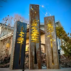 three tall metal sculptures with trees on them in front of a house at night time