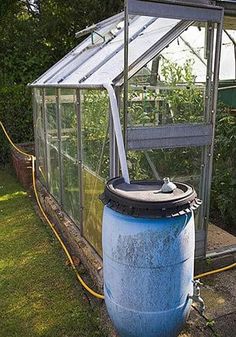 a large blue barrel sitting in the grass next to a small building with a greenhouse on top