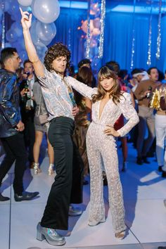 a man standing next to a woman on top of a dance floor with balloons in the air