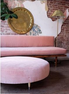 a pink couch sitting in front of a brick wall next to a wooden table with a plant on it