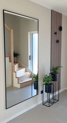 a mirror sitting on the side of a wall next to potted plants and a stair case