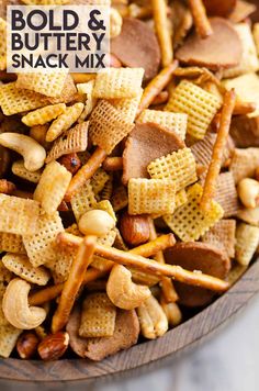 a wooden bowl filled with cheetos, peanuts and buttery snack mix on top of a marble counter