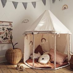 a white tent sitting on top of a wooden floor next to a basket filled with pillows