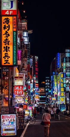 a city street filled with lots of neon signs and people walking down the road at night