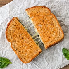 a sandwich cut in half sitting on top of a piece of paper with basil leaves