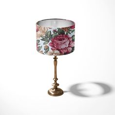 a lamp shade with flowers on it and a gold base is shown in front of a white background