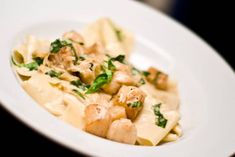 a white plate topped with pasta covered in sauce and spinach garnished with parsley