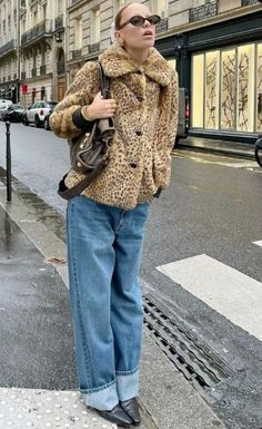 a woman is standing on the sidewalk with her hand in her pocket and wearing a leopard print coat