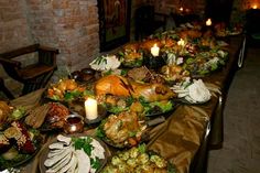 a long table with many plates of food on it and lit candles in the background