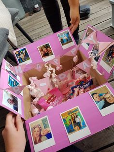 a pink box filled with photos and pictures on top of a wooden table next to a person