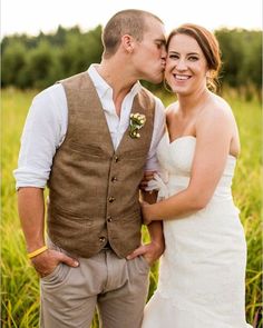 a bride and groom kissing in the middle of a field with tall grass behind them