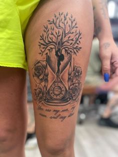 a woman's leg with a clock and tree tattoo on the side of her thigh