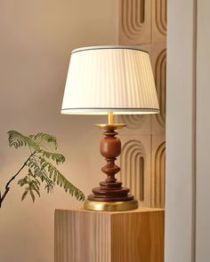 a lamp sitting on top of a wooden table next to a potted fern plant