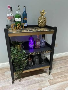 a black and gold bar cart with liquor bottles on the top, two glasses sitting on it