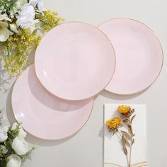 three pink plates sitting on top of a table next to white flowers and a napkin