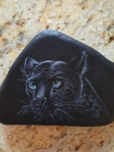 a close up of a rock with a black cat on it's face and blue eyes