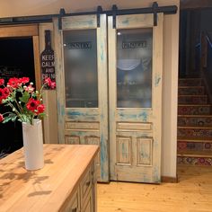 a vase filled with red flowers sitting on top of a wooden table next to a doorway