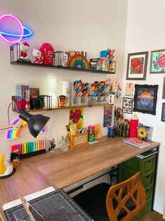 a desk with many items on it and some pictures hanging above the desk, in front of a white wall